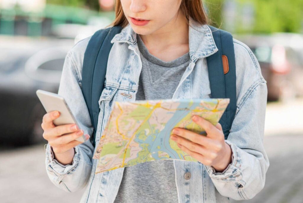 Mujer buscando algo en su celular en una mano y un mapa en la otra