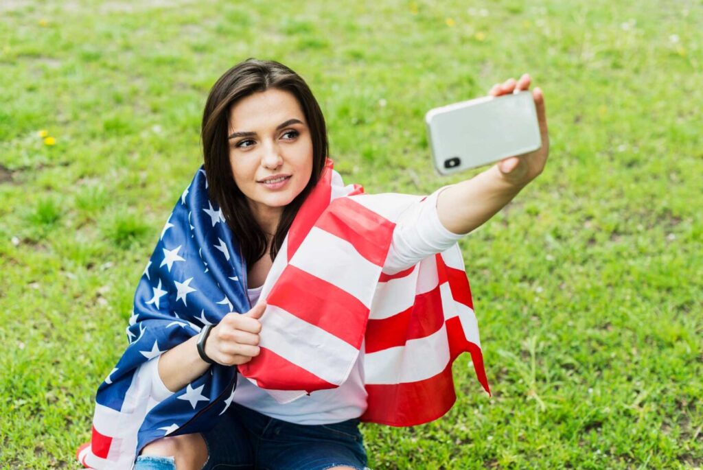 Mujer sentada tomándose una selfie con la bandera de Estados Unidos como capa