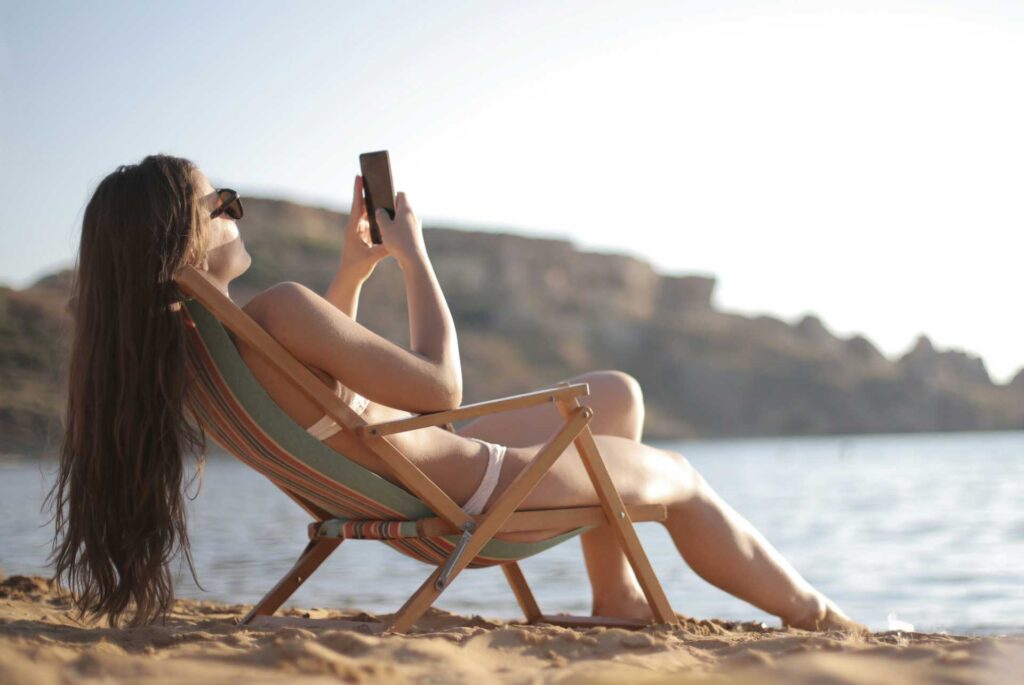 Mujer sentada en la playa disfrutando del sol y su celular