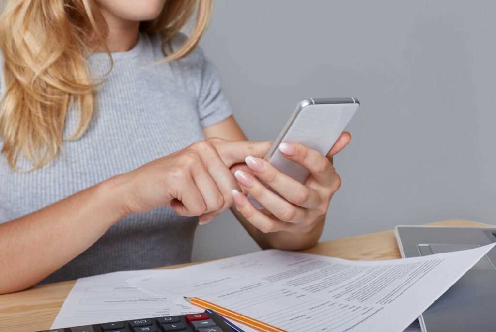 Mujer sostiene celular y anota en su libreta